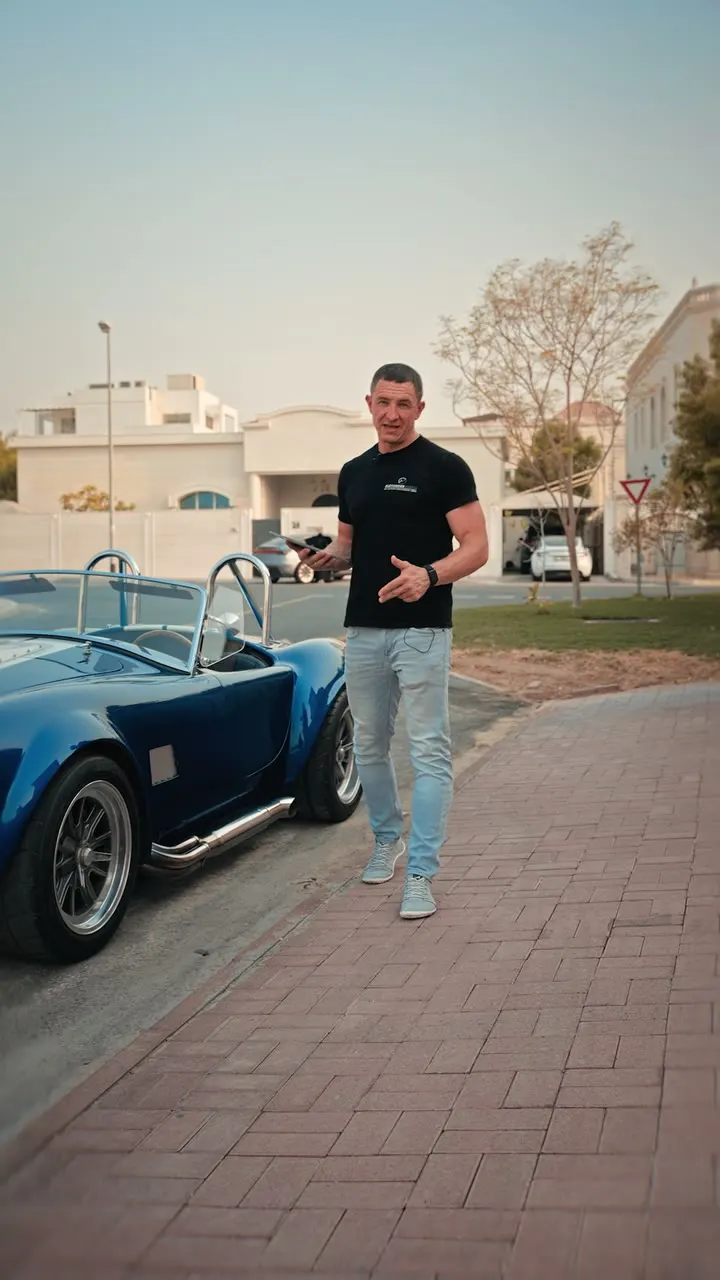Kfz-Sachverständiger Alexander Fertig mit Tablet neben einer blauen Factory Five Cobra bei der Fahrzeugbewertung